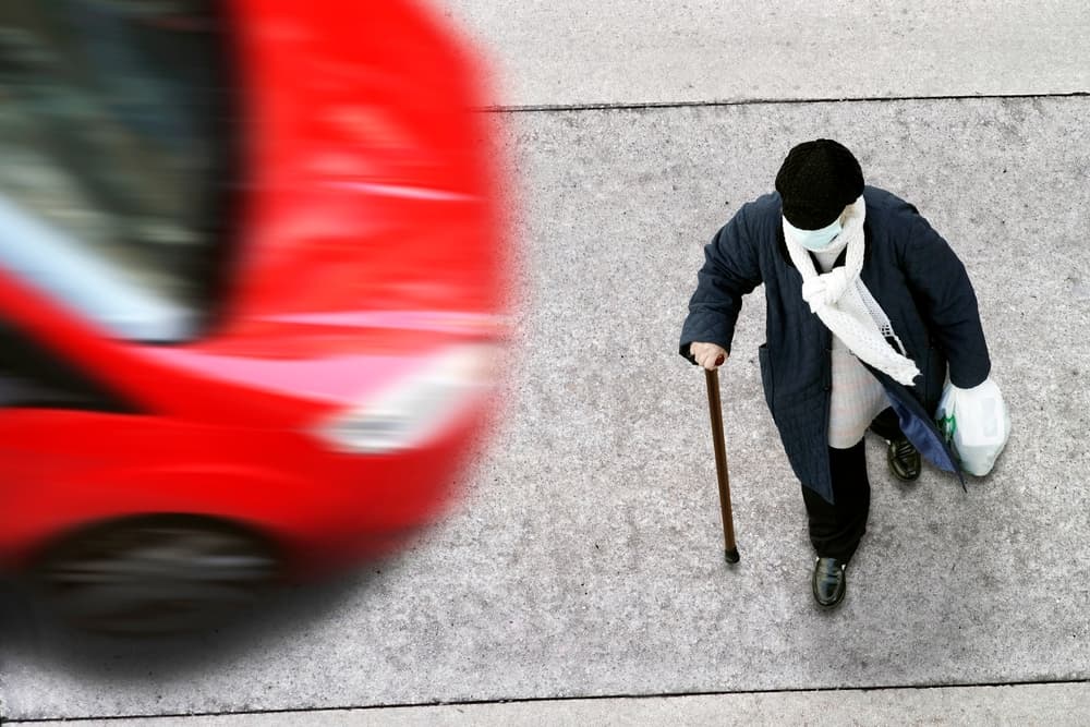 Elderly woman crossing the road in the city street without taking precautions and a car may hit her