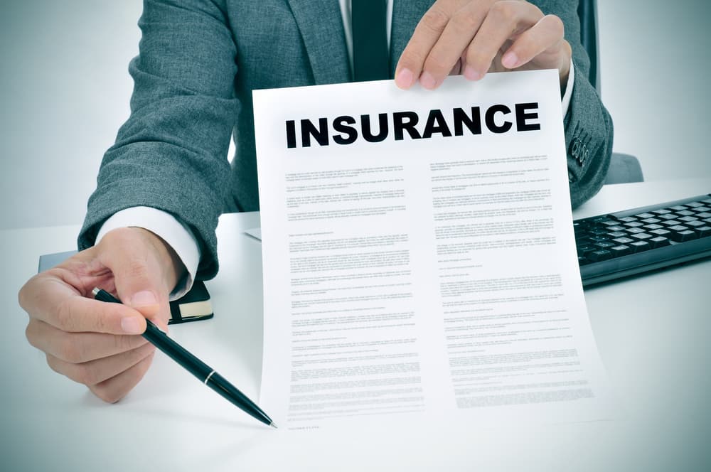 A young man in suit in his office showing an insurance policy and pointing with a pen