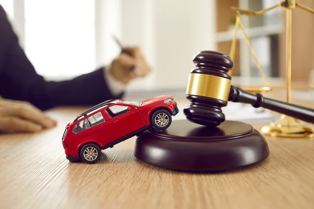 Red toy car on a desk beside a gavel and sound block, symbolizing car accidents, legal cases, and lawyer services.