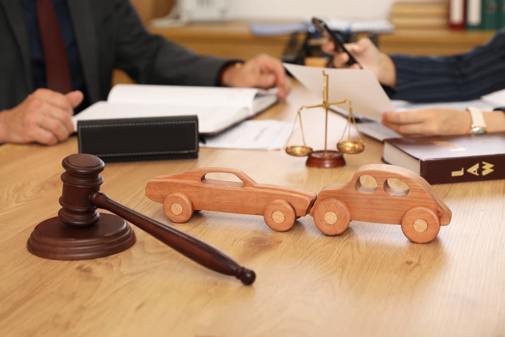 Wooden car models, gavel, and scales of justice symbolize legal consultation for car accident cases.